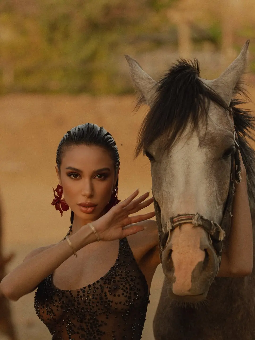 Close fashion portrait beside a horse, hand near its face.