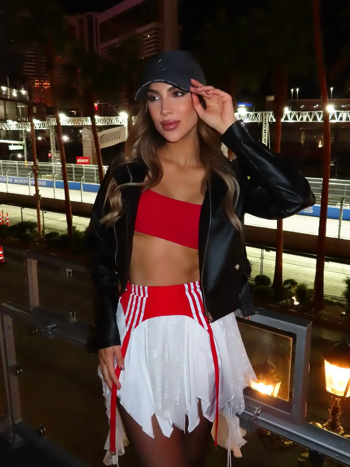 Red top, dark jacket and white-fringe skirt beside night track.
